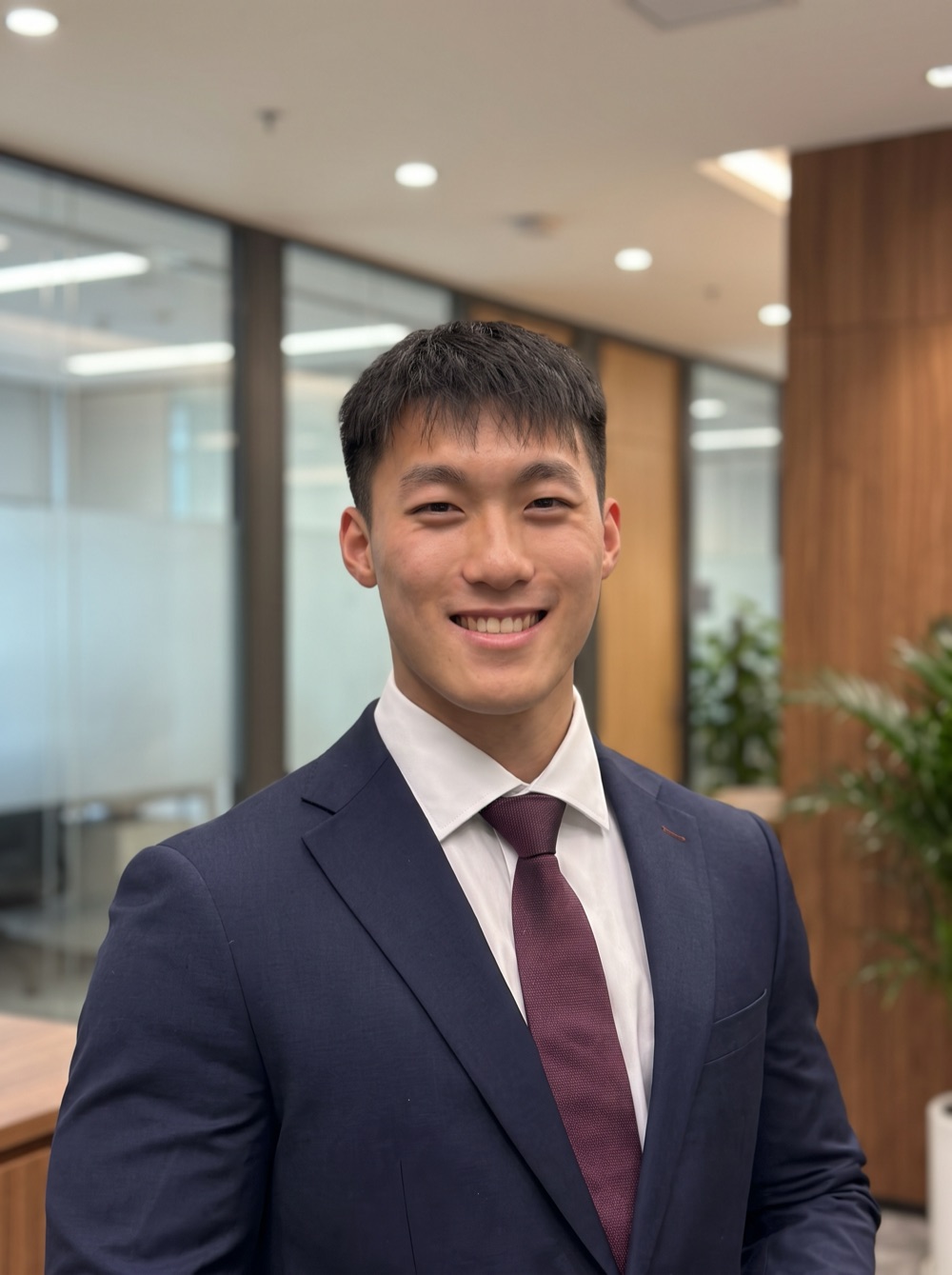 Evan Yap smiling, in a navy suit and burgundy tie, standing in an office.